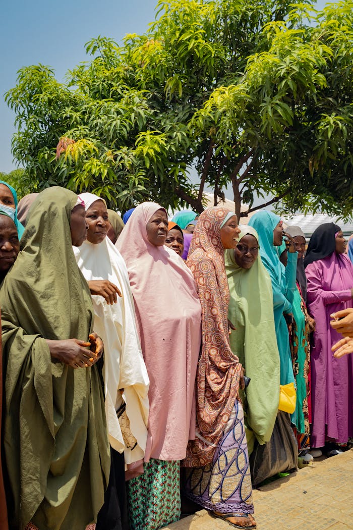 A group of women in colorful hijabs gathering under a tree on a sunny day.