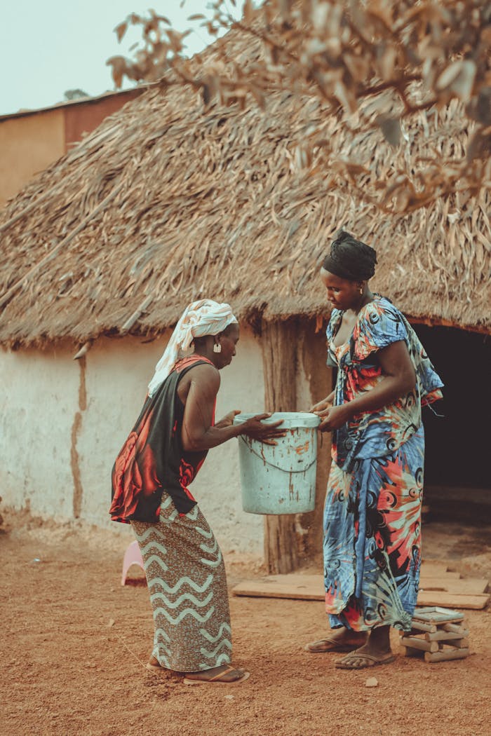 Two women collaborating in their daily village chores near a traditional hut.